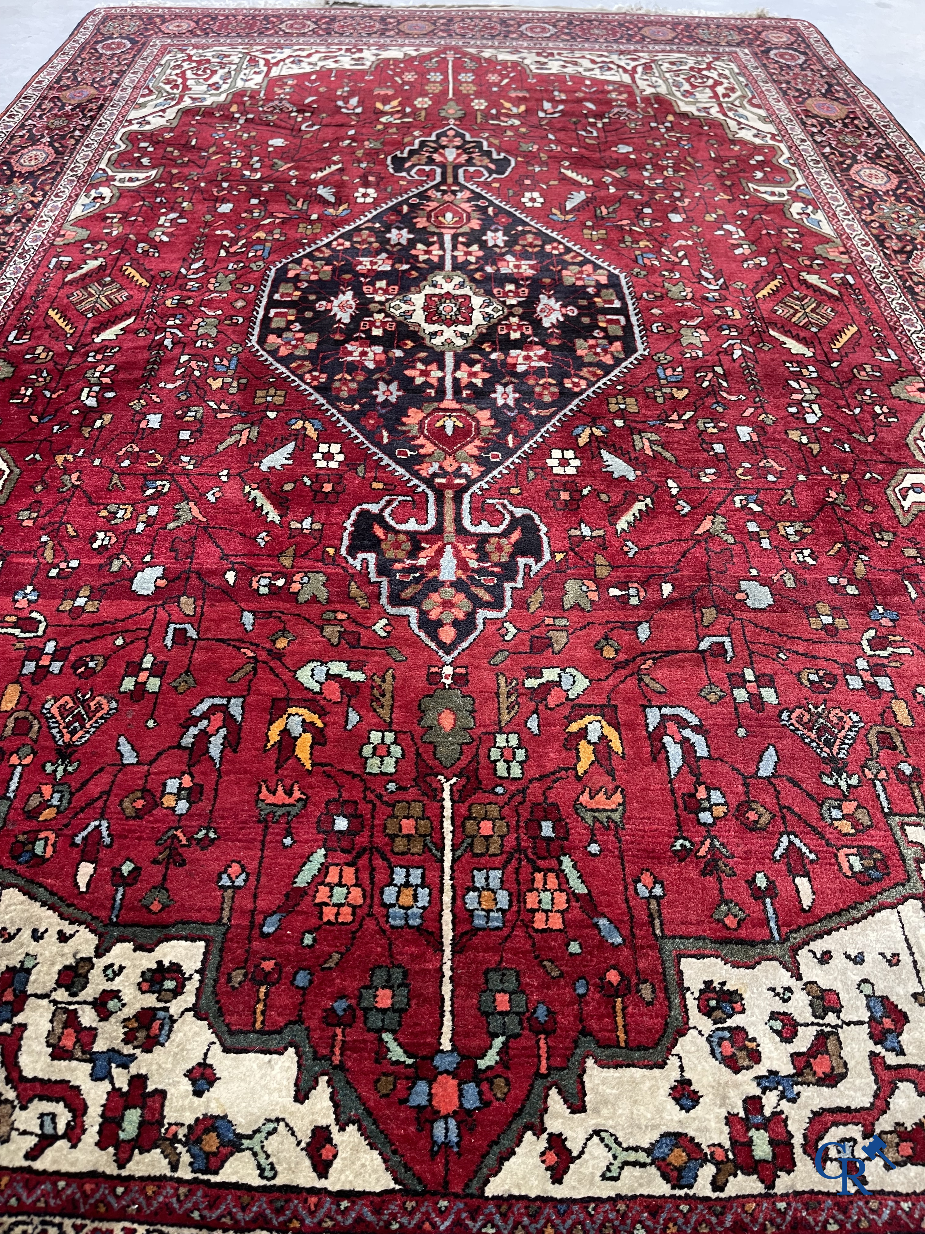 Tapis persan: Un tapis oriental finement noué avec un fond rouge foncé.