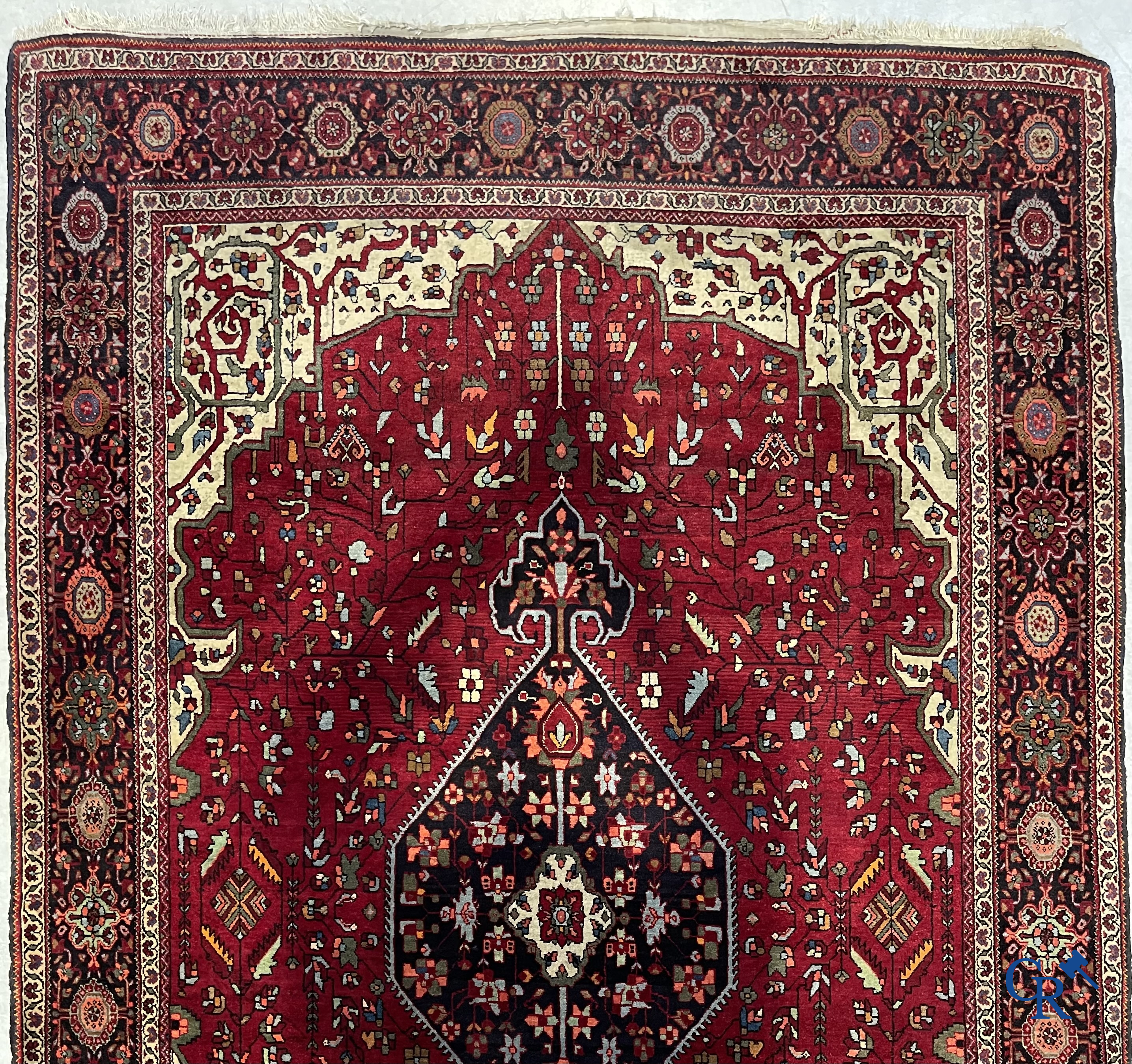 Tapis persan: Un tapis oriental finement noué avec un fond rouge foncé.