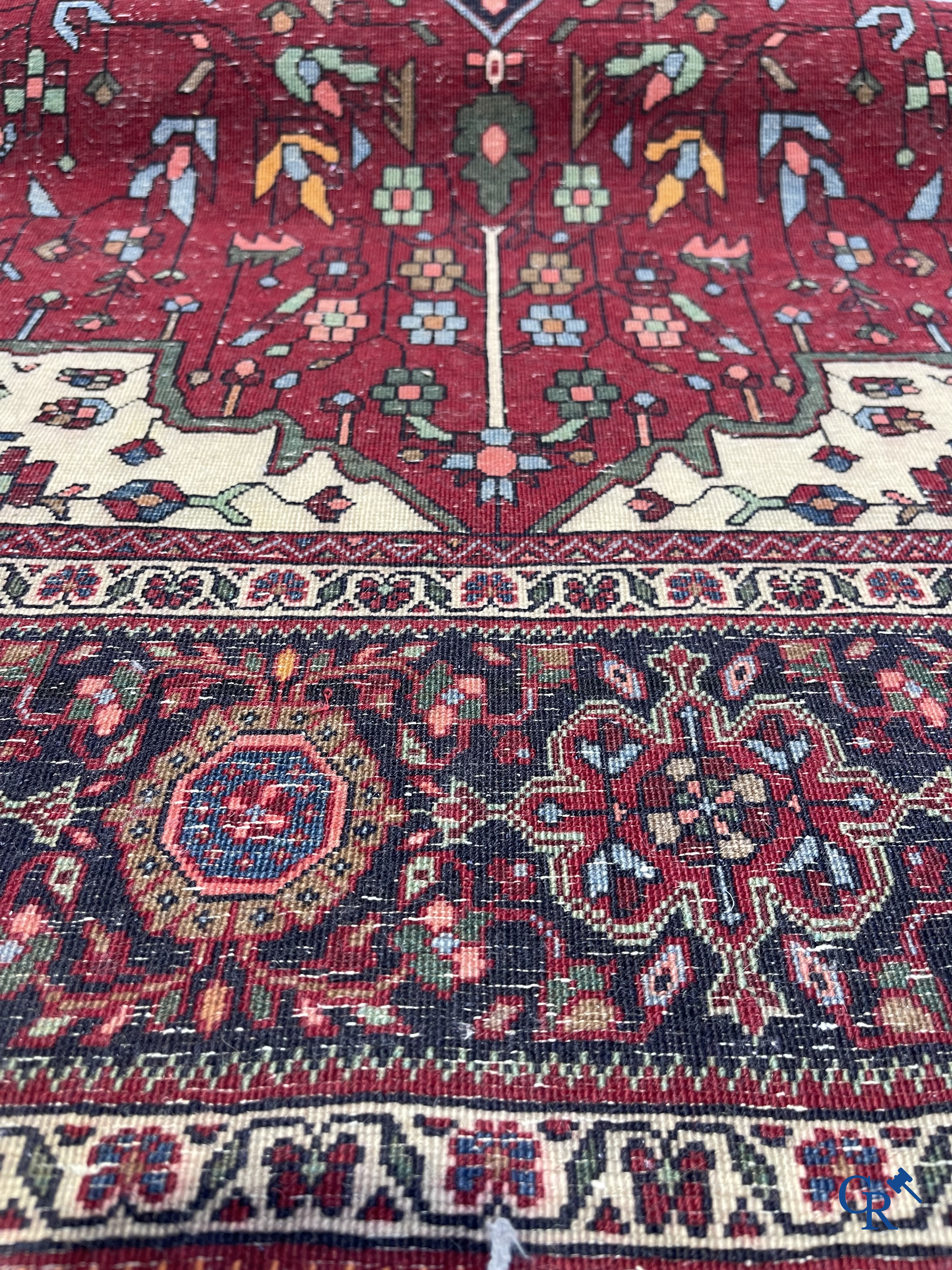 Tapis persan: Un tapis oriental finement noué avec un fond rouge foncé.