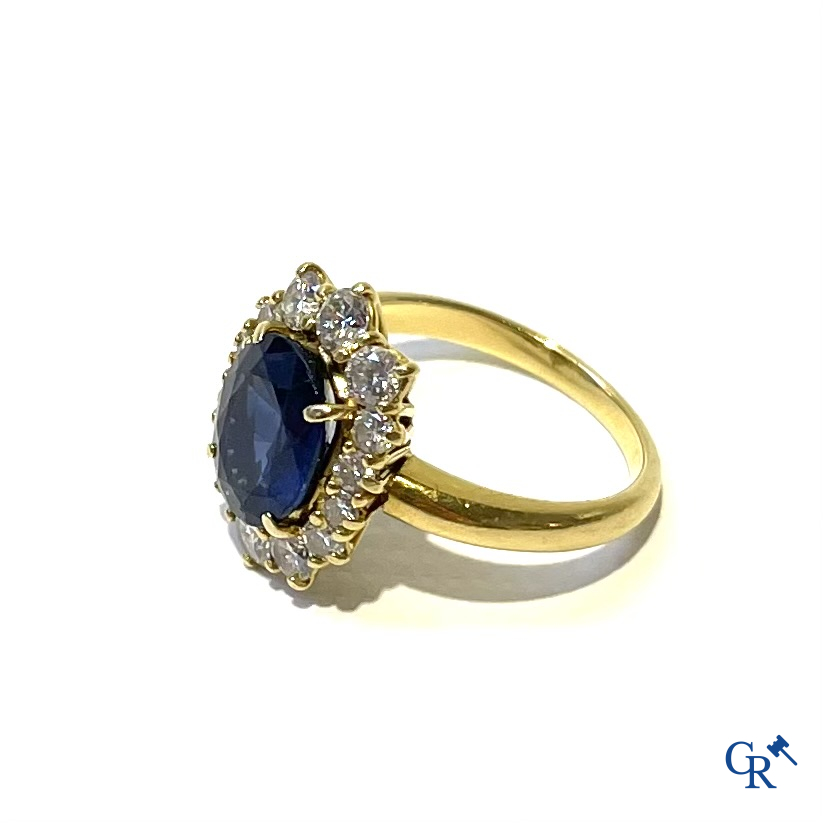 Juwelen. Ring in geelgoud 750°/00 bezet met een centrale blauwe saffier omringd door 14 kleine diamanten.