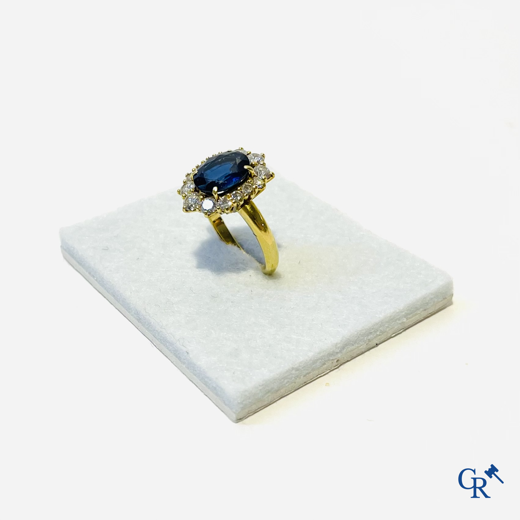 Juwelen. Ring in geelgoud 750°/00 bezet met een centrale blauwe saffier omringd door 14 kleine diamanten.