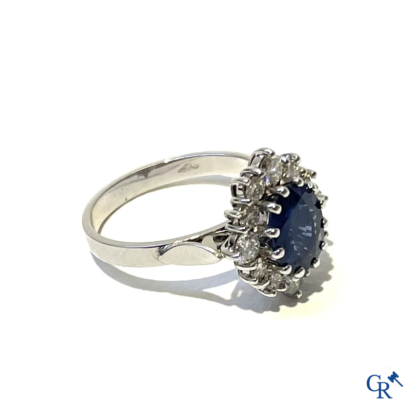 Juwelen. Ring in witgoud 750°/00 bezet met een centrale blauwe saffier omringd door 12 kleine diamanten.