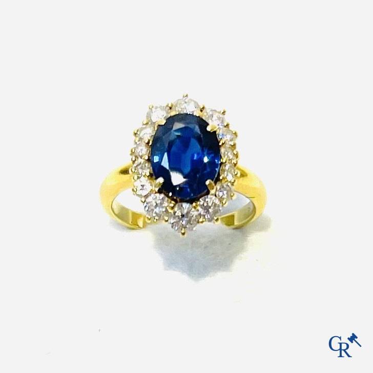 Juwelen. Ring in geelgoud 750°/00 bezet met een centrale blauwe saffier omringd door 14 kleine diamanten.