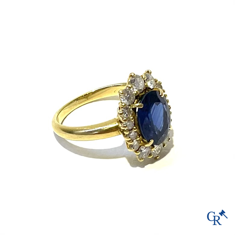 Juwelen. Ring in geelgoud 750°/00 bezet met een centrale blauwe saffier omringd door 14 kleine diamanten.