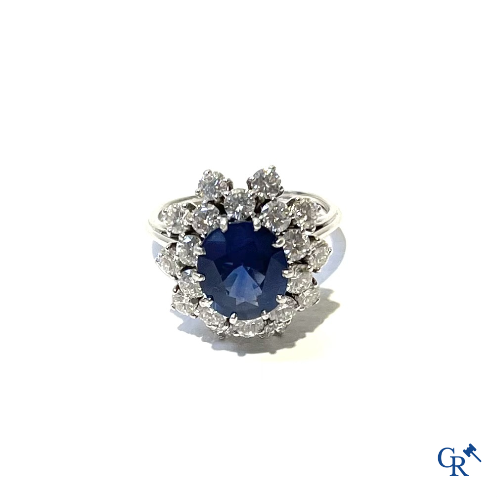 Juwelen. Ring in witgoud 750°/00 bezet met een centrale blauwe saffier omringd door 20 kleine diamanten.