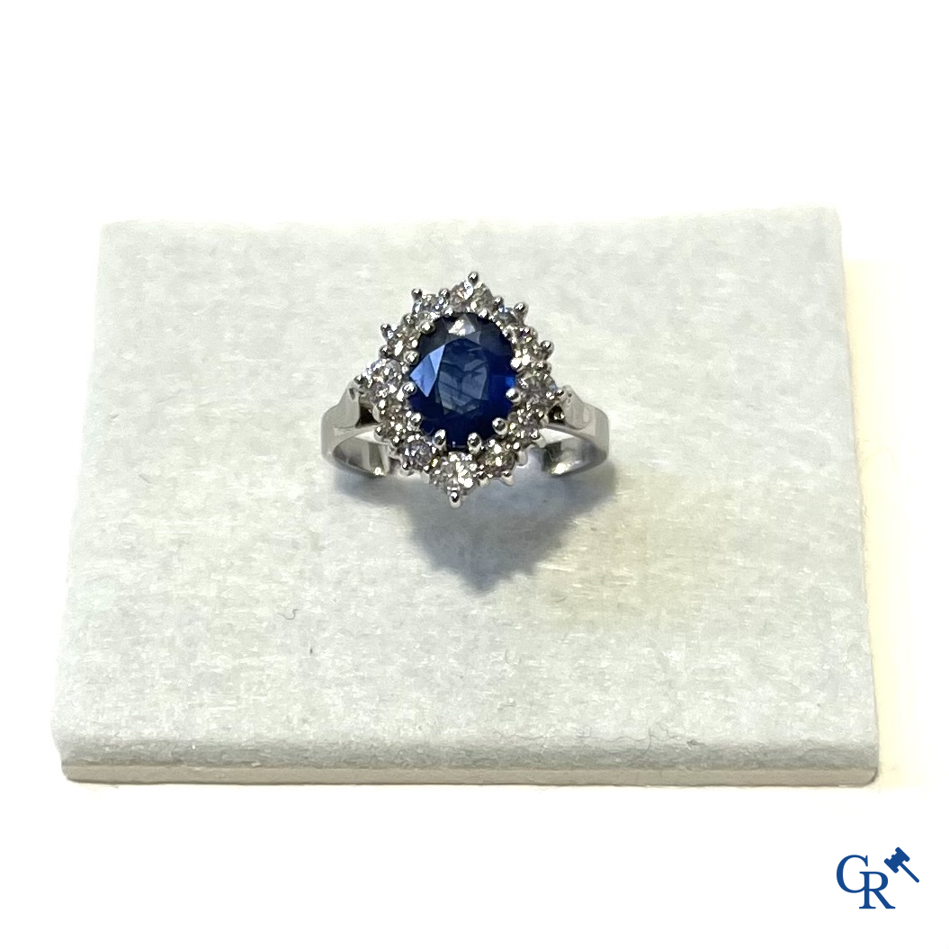 Juwelen. Ring in witgoud 750°/00 bezet met een centrale blauwe saffier omringd door 12 kleine diamanten.
