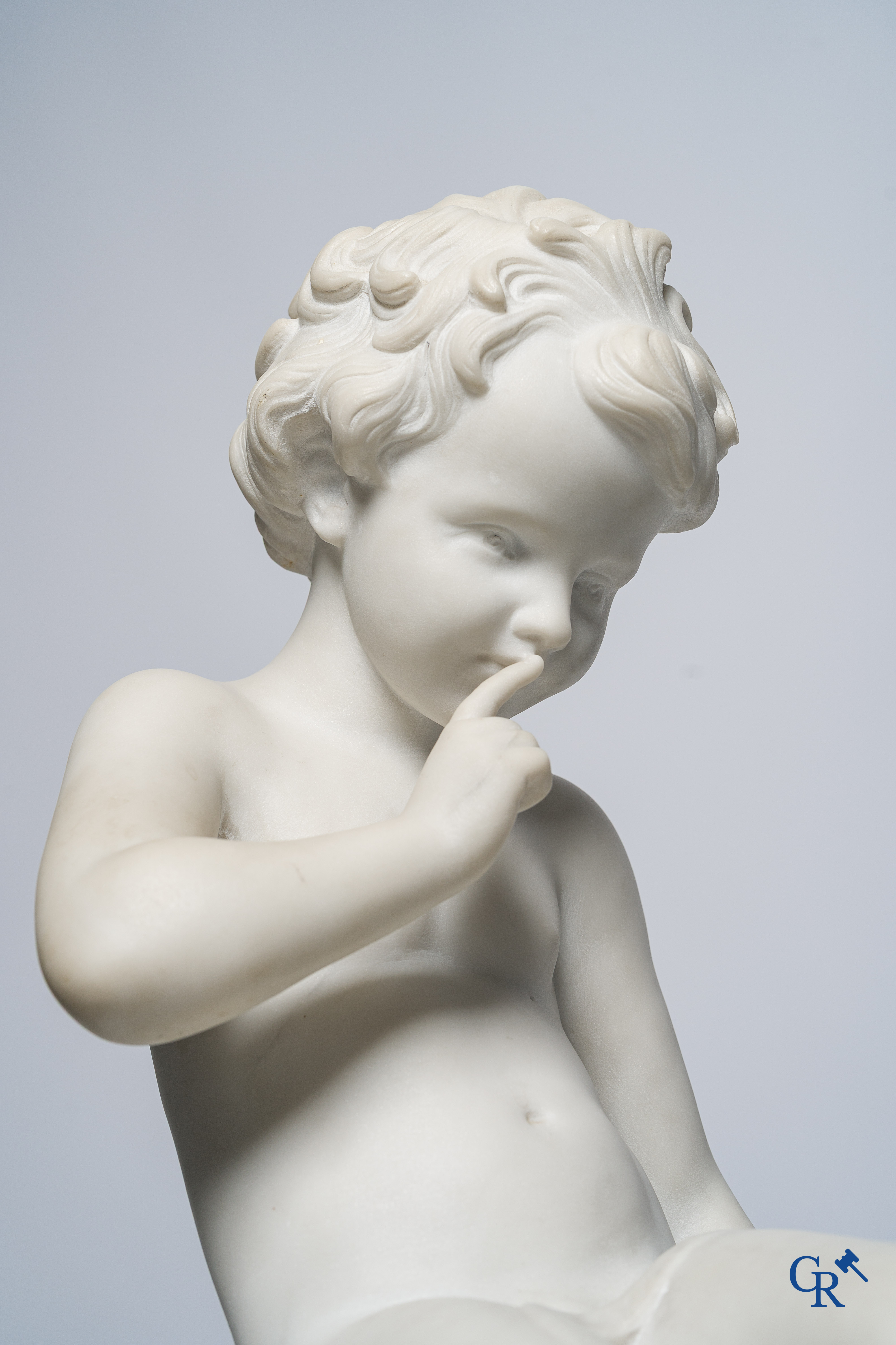 Representation of a seated cupid in white Carrara marble. In the style of Jean-Baptiste Pigalle. Around 1900..