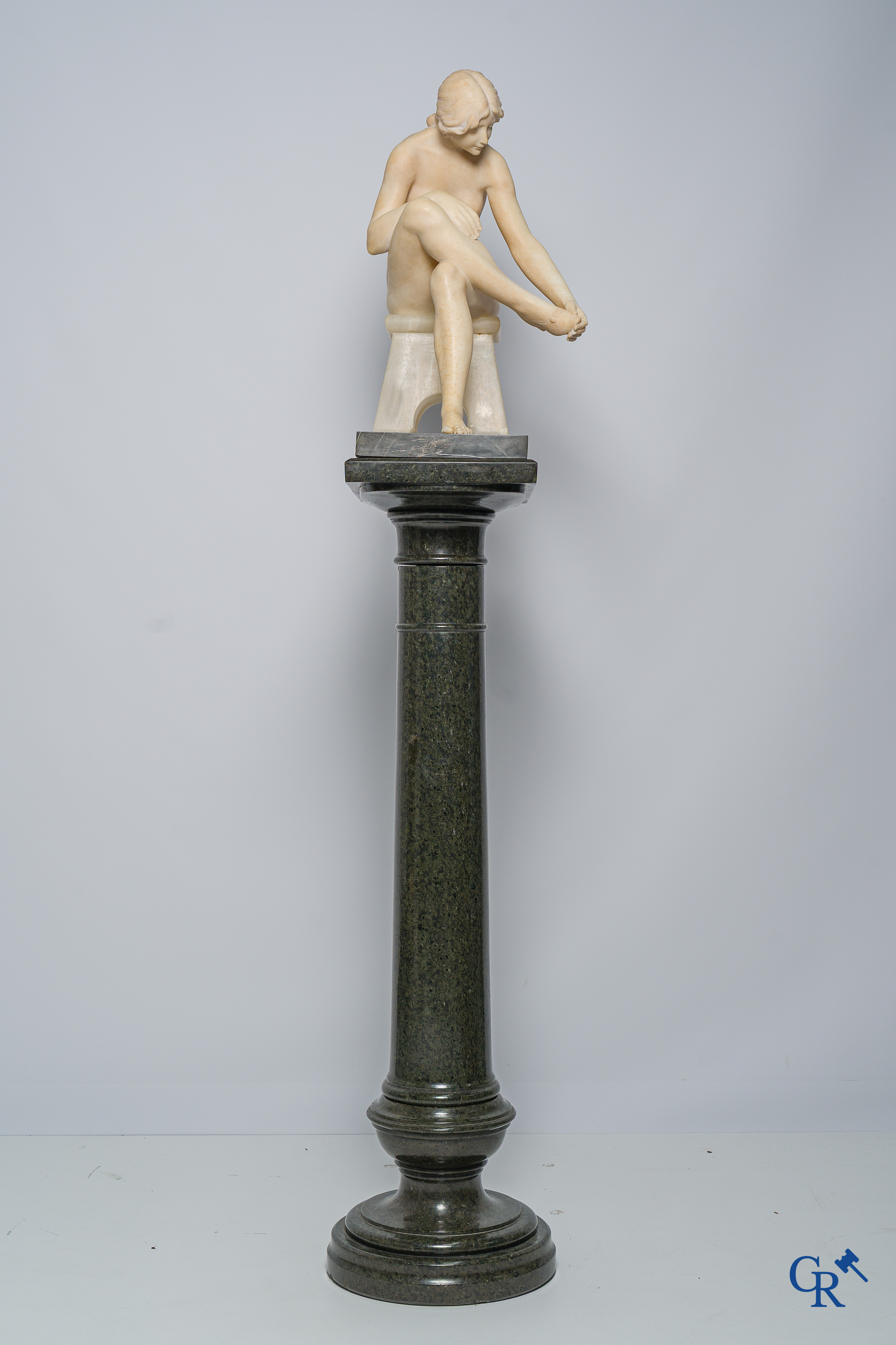 Art Nouveau. Marble statue of a sitting young lady on a chair. Associated pedestal in serpentine. Circa 1910.