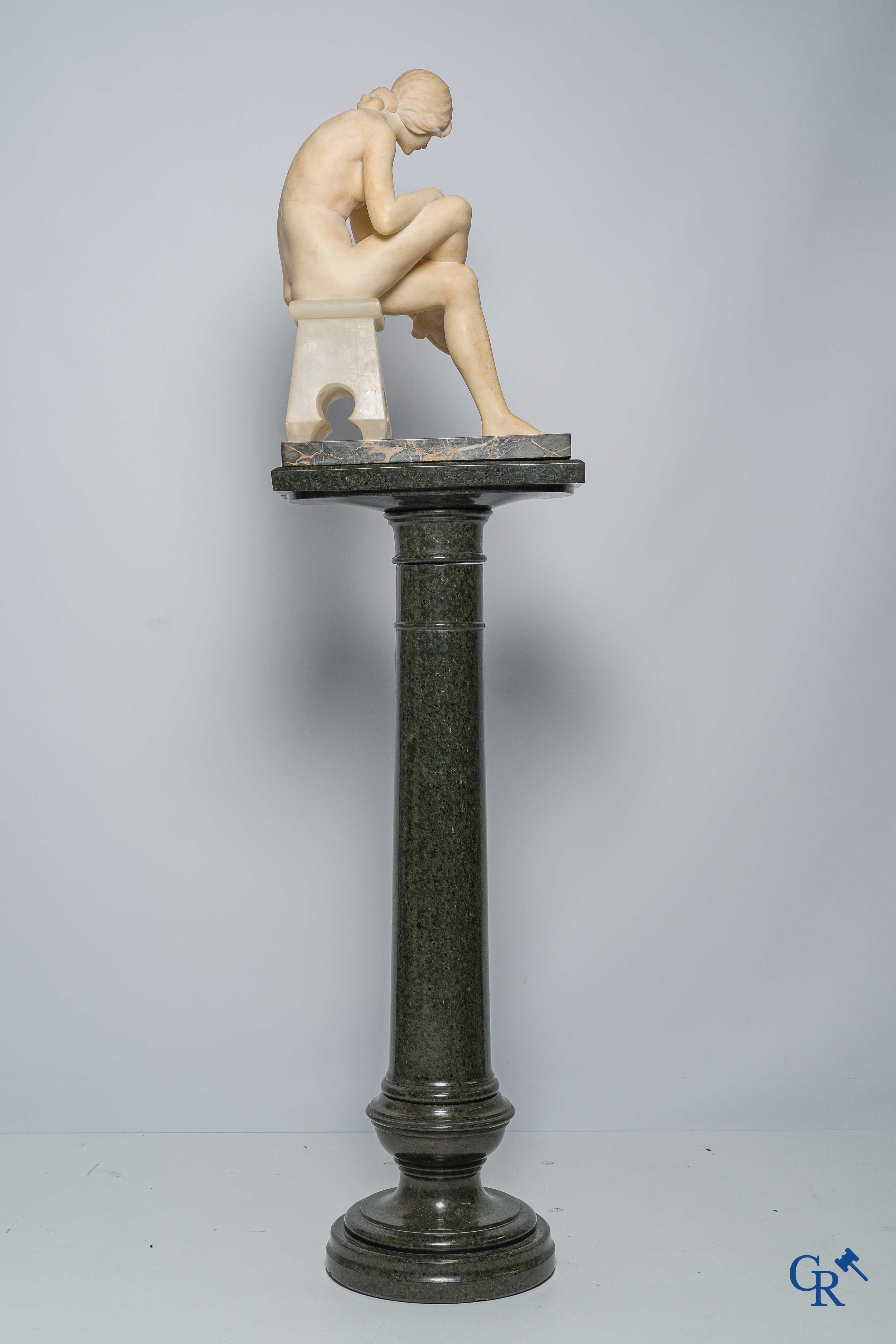Art Nouveau. Marble statue of a sitting young lady on a chair. Associated pedestal in serpentine. Circa 1910.