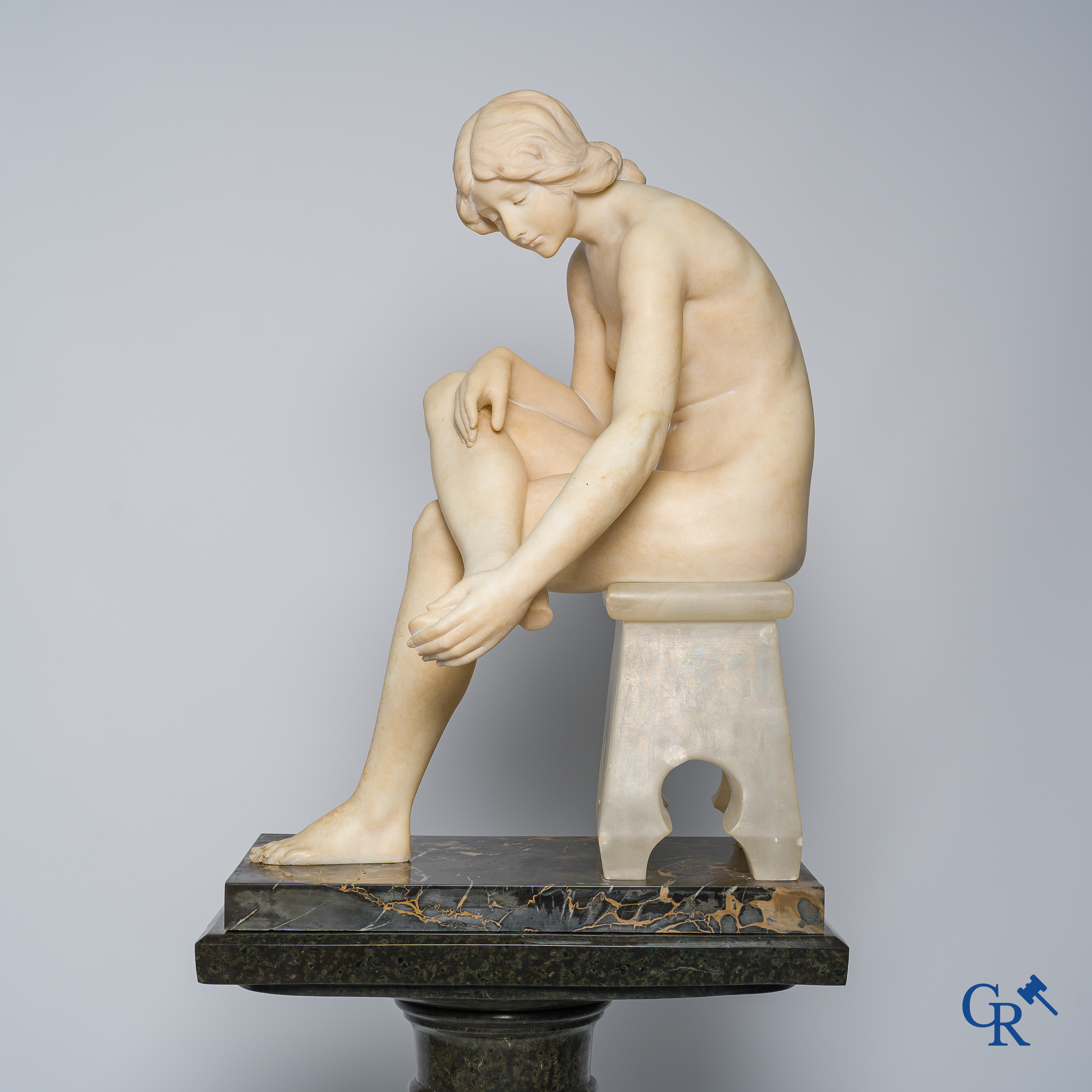Art Nouveau. Marble statue of a sitting young lady on a chair. Associated pedestal in serpentine. Circa 1910.