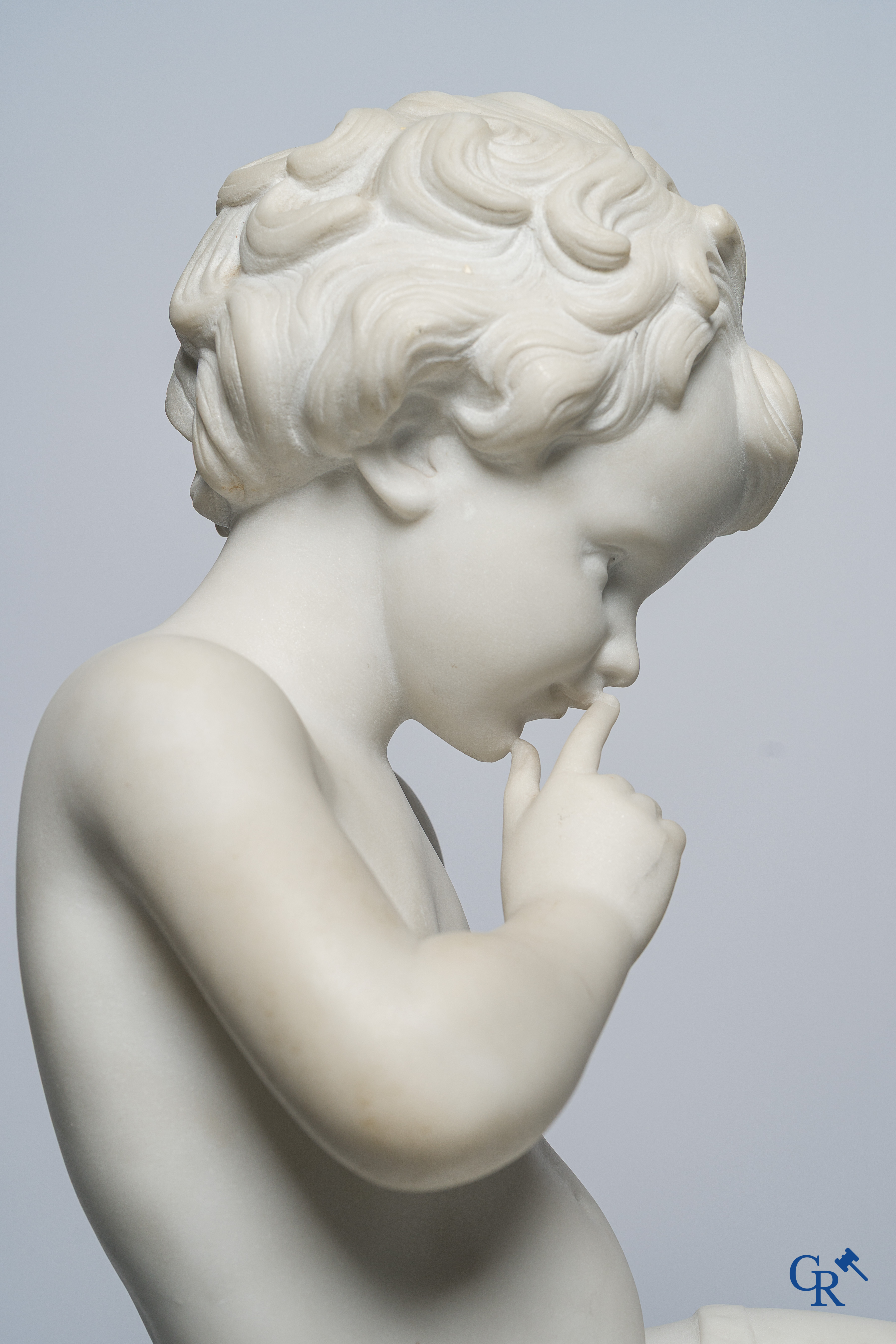 Representation of a seated cupid in white Carrara marble. In the style of Jean-Baptiste Pigalle. Around 1900..
