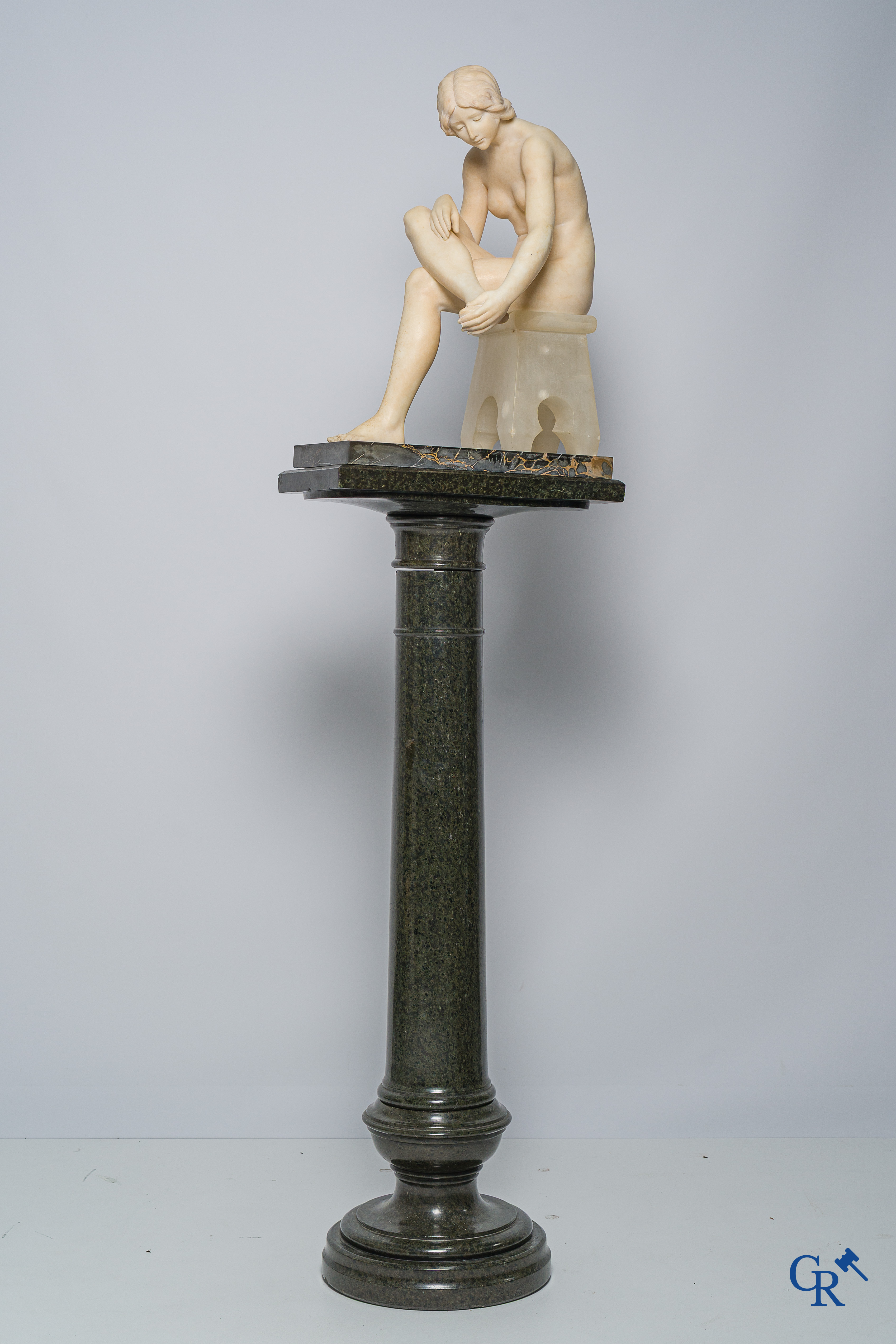Art Nouveau. Marble statue of a sitting young lady on a chair. Associated pedestal in serpentine. Circa 1910.