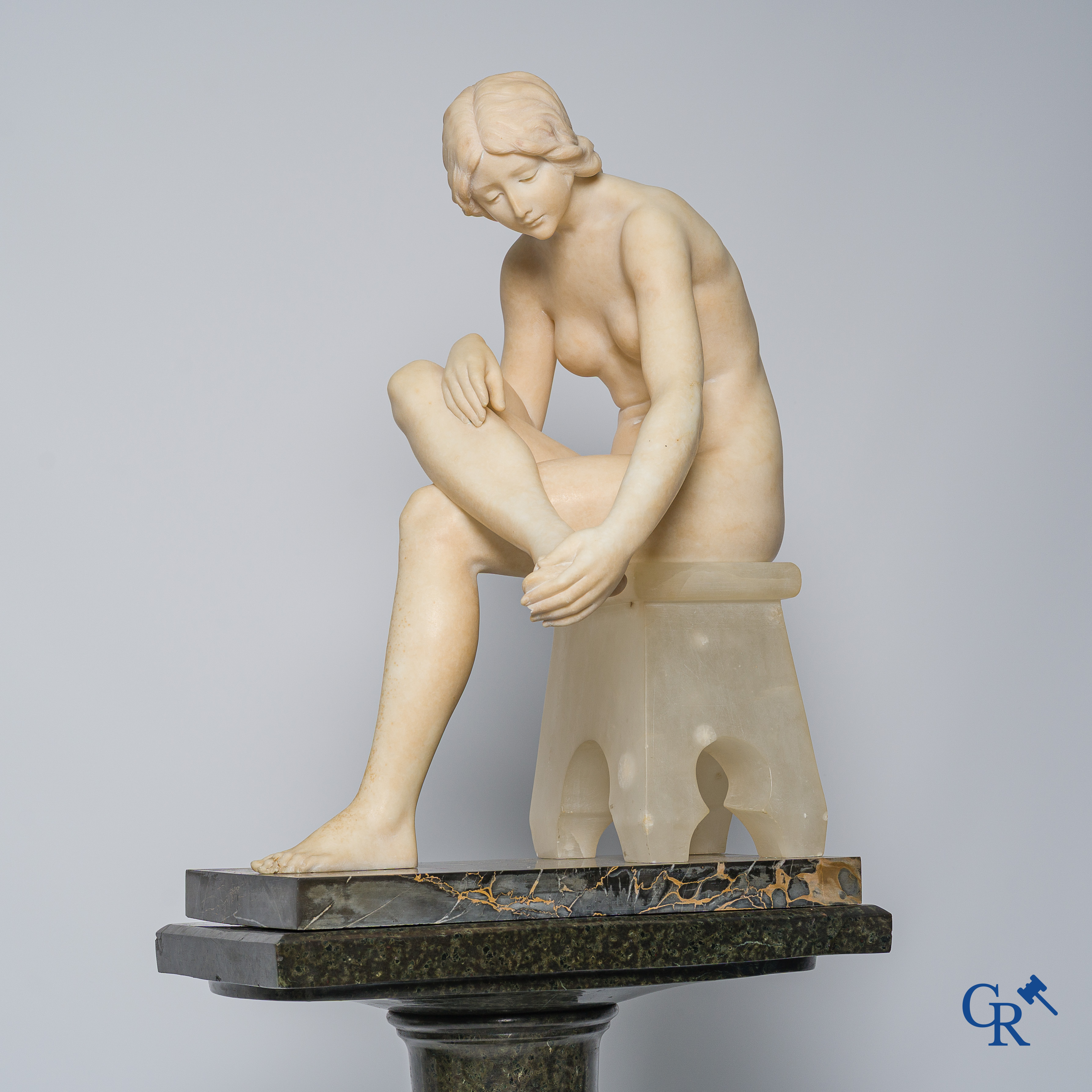 Art Nouveau. Marble statue of a sitting young lady on a chair. Associated pedestal in serpentine. Circa 1910.
