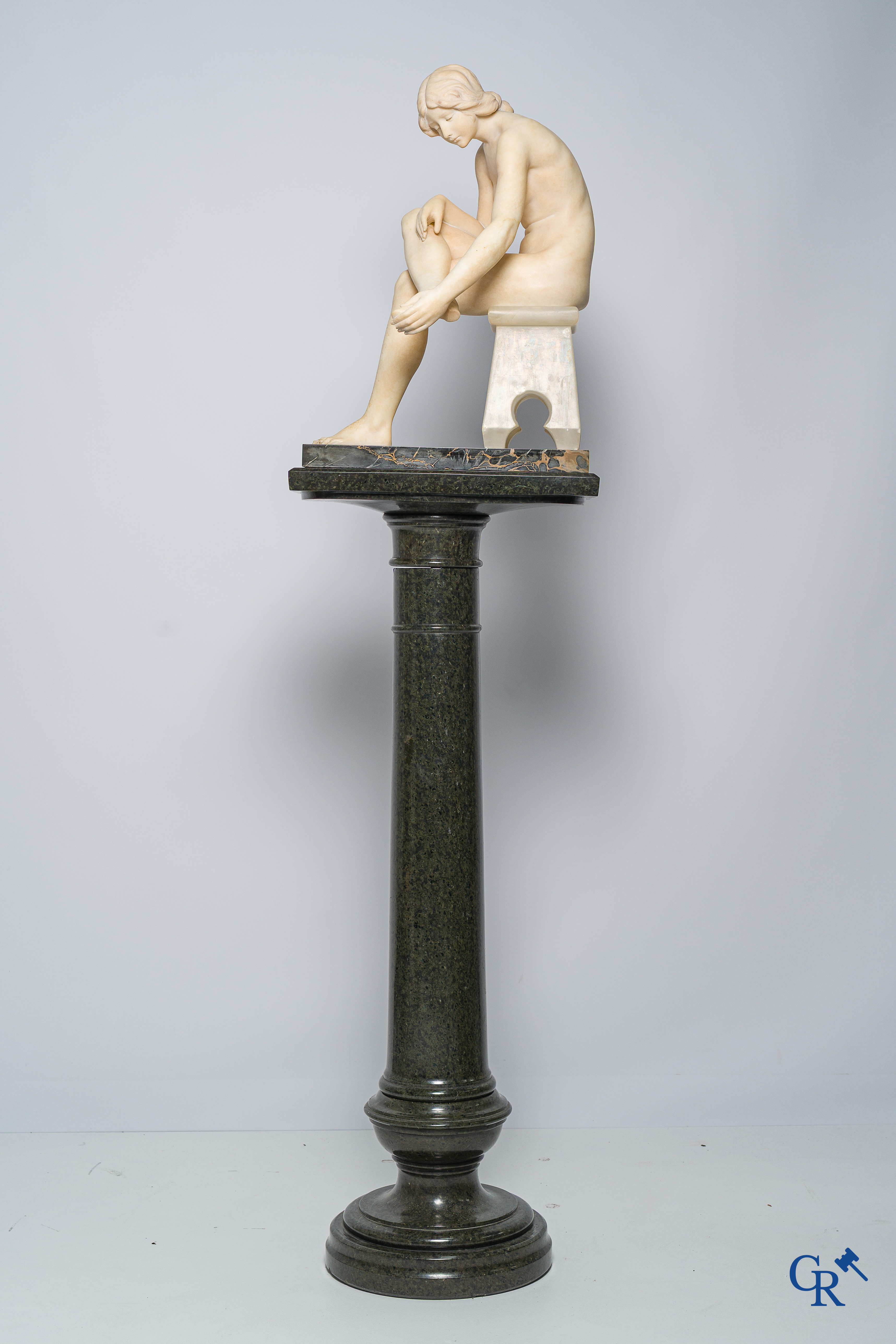 Art Nouveau. Marble statue of a sitting young lady on a chair. Associated pedestal in serpentine. Circa 1910.