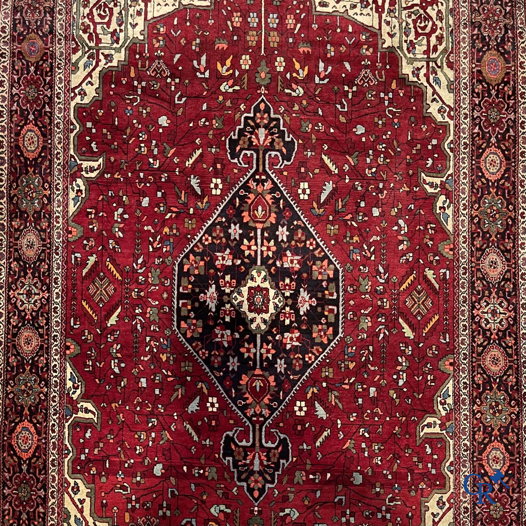 Tapis persan: Un tapis oriental finement noué avec un fond rouge foncé.