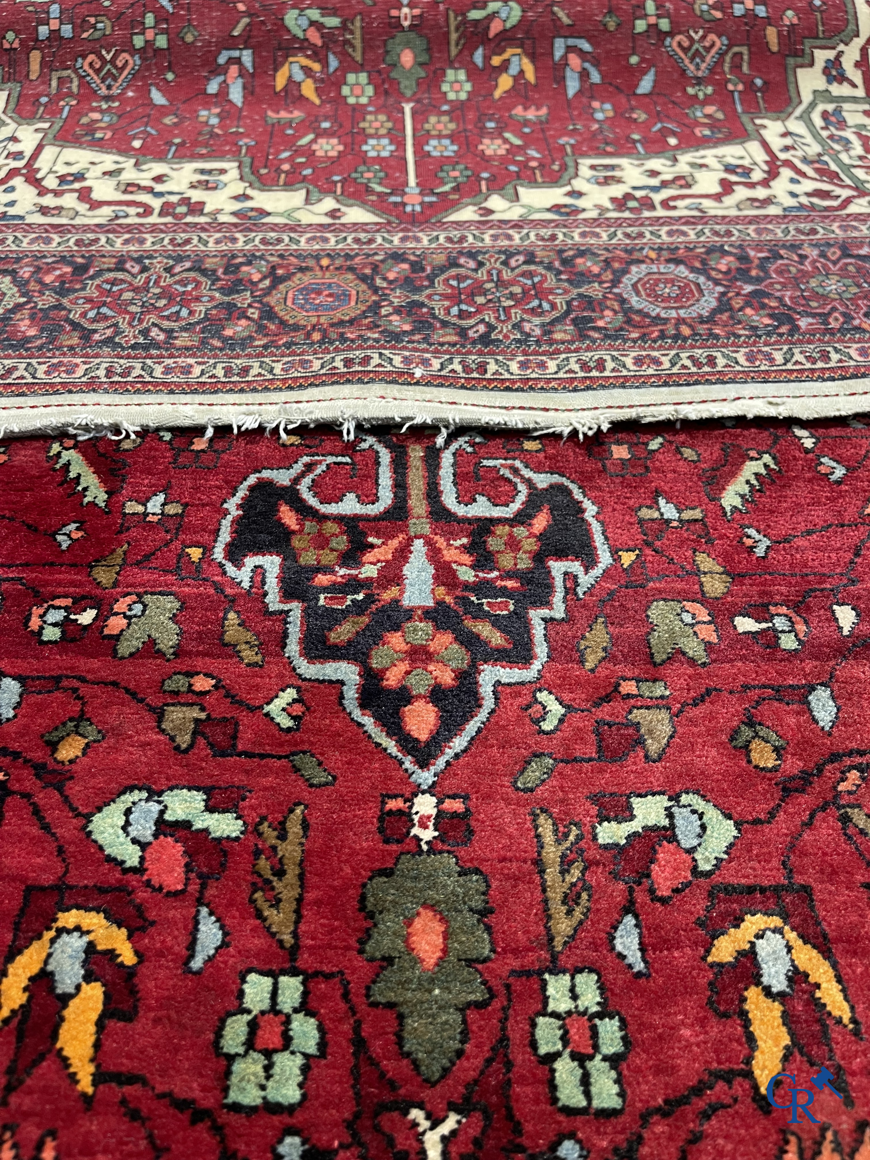 Tapis persan: Un tapis oriental finement noué avec un fond rouge foncé.