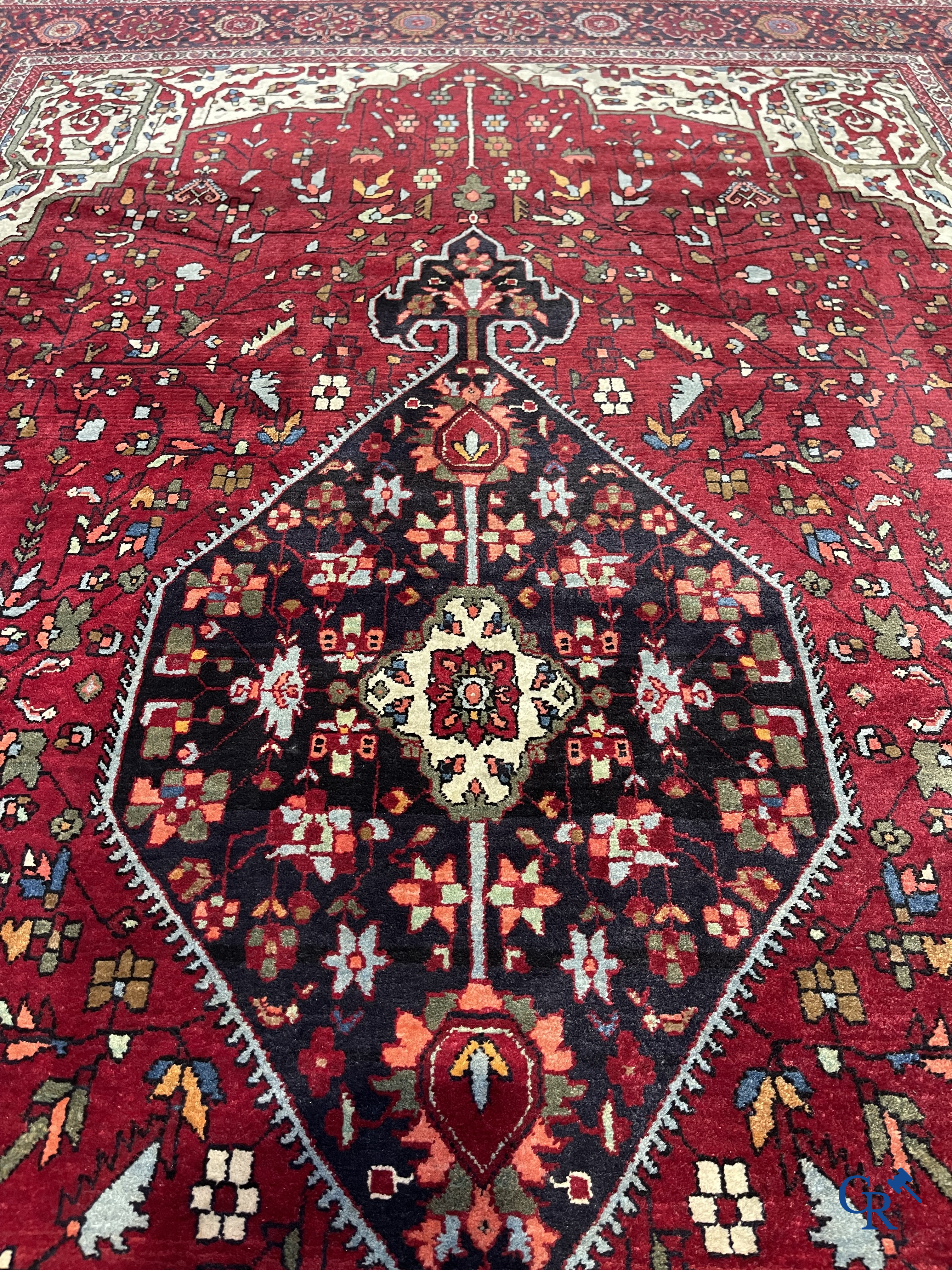 Tapis persan: Un tapis oriental finement noué avec un fond rouge foncé.