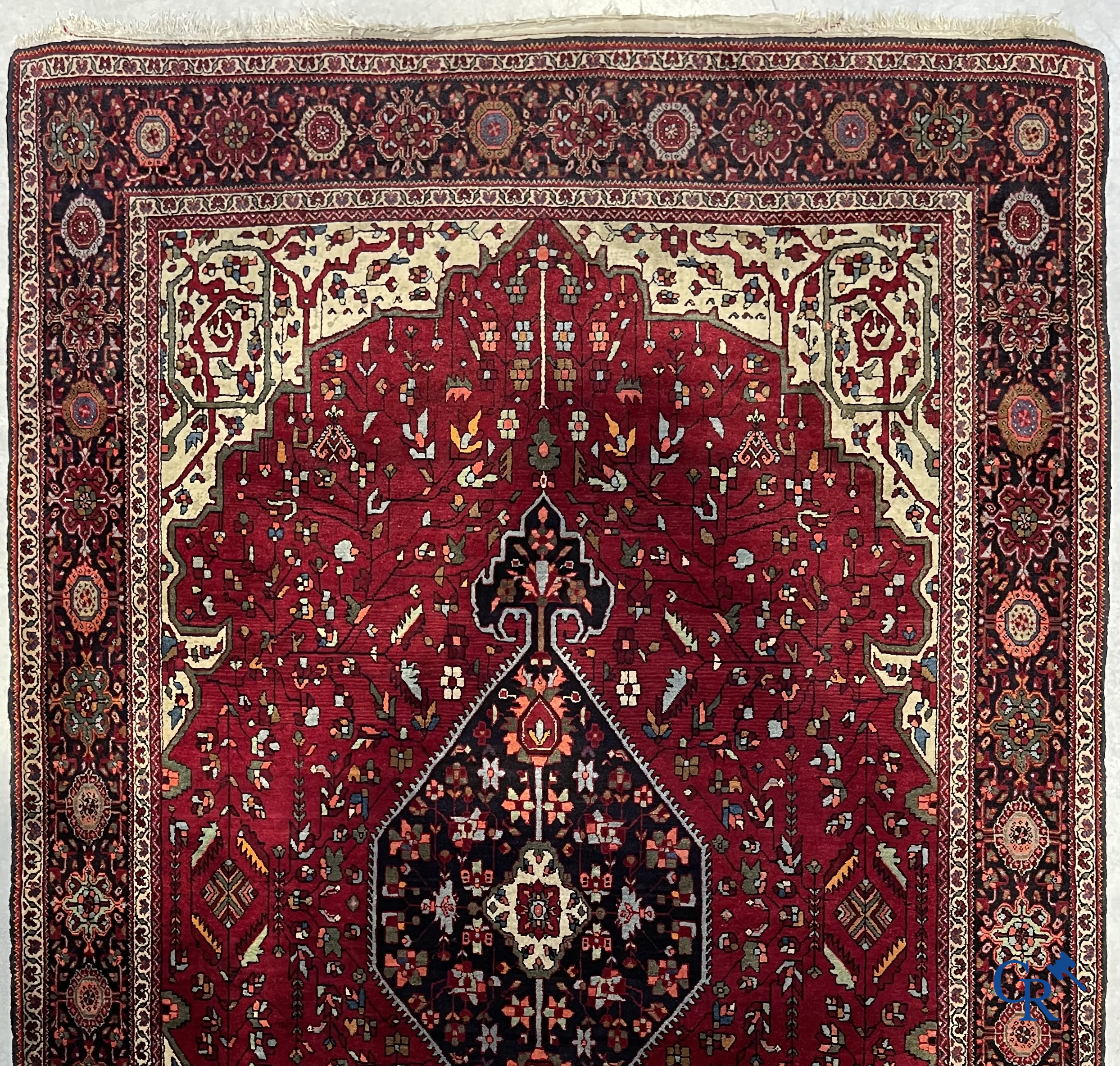 Tapis persan: Un tapis oriental finement noué avec un fond rouge foncé.