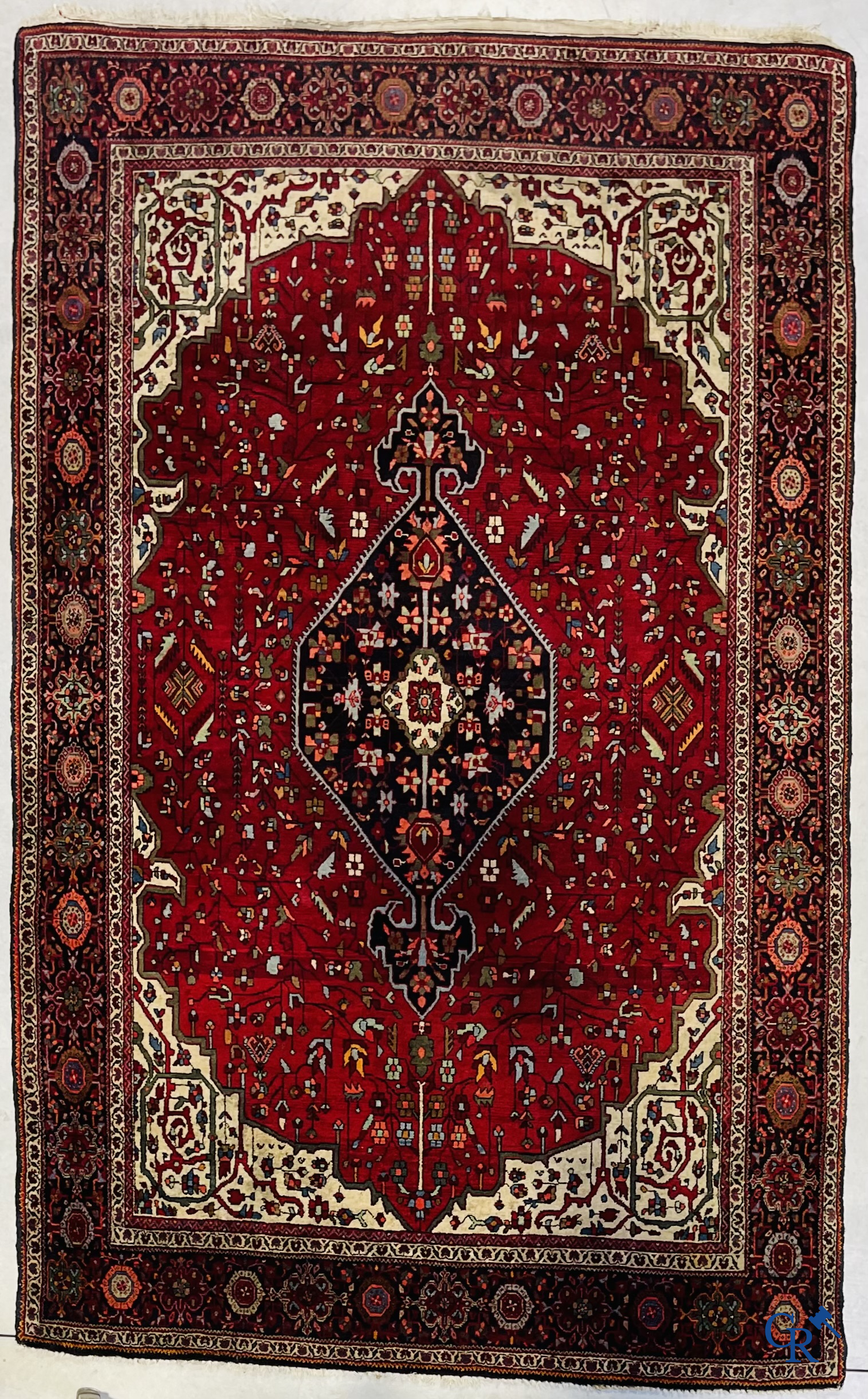 Tapis persan: Un tapis oriental finement noué avec un fond rouge foncé.