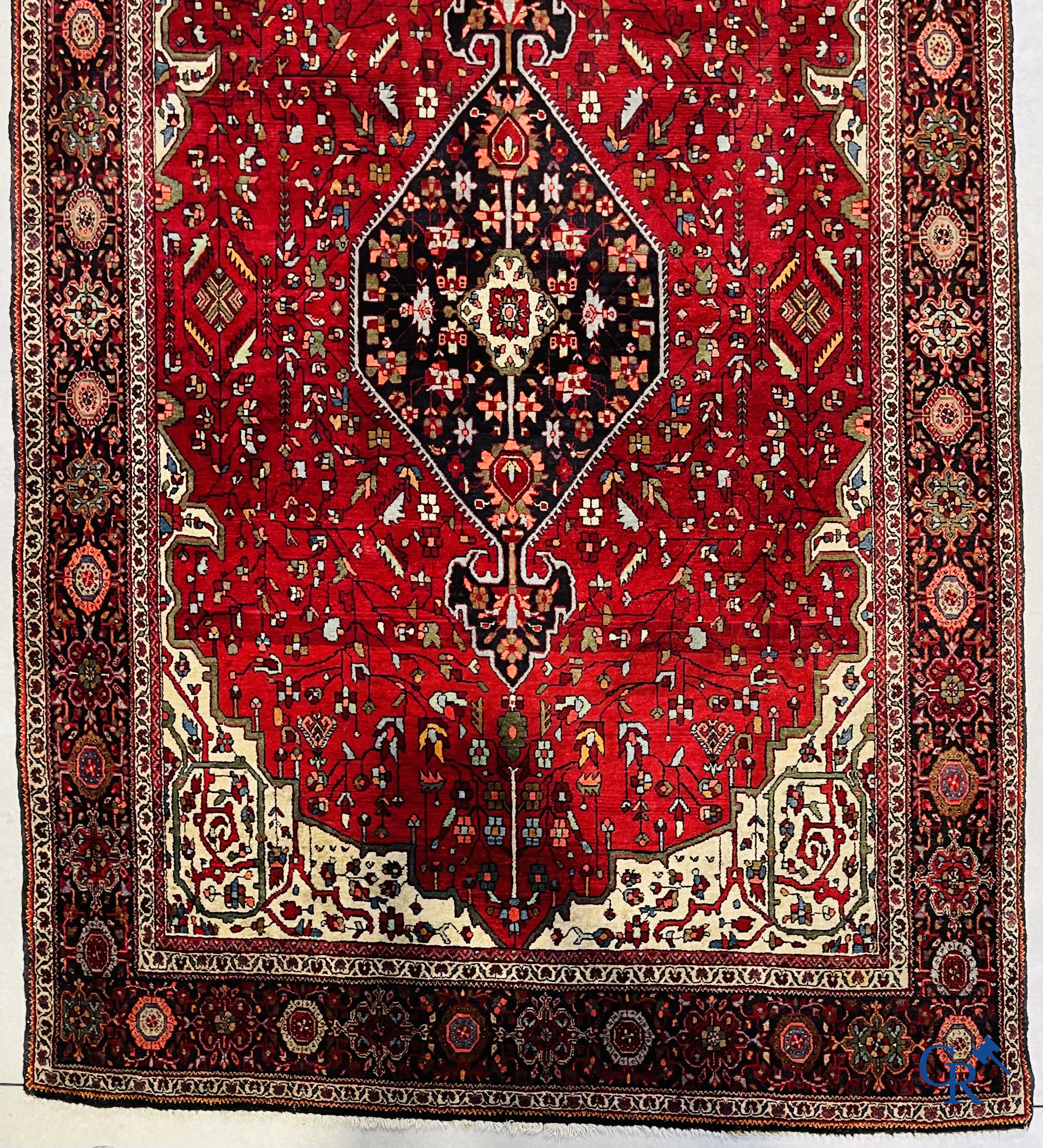 Tapis persan: Un tapis oriental finement noué avec un fond rouge foncé.