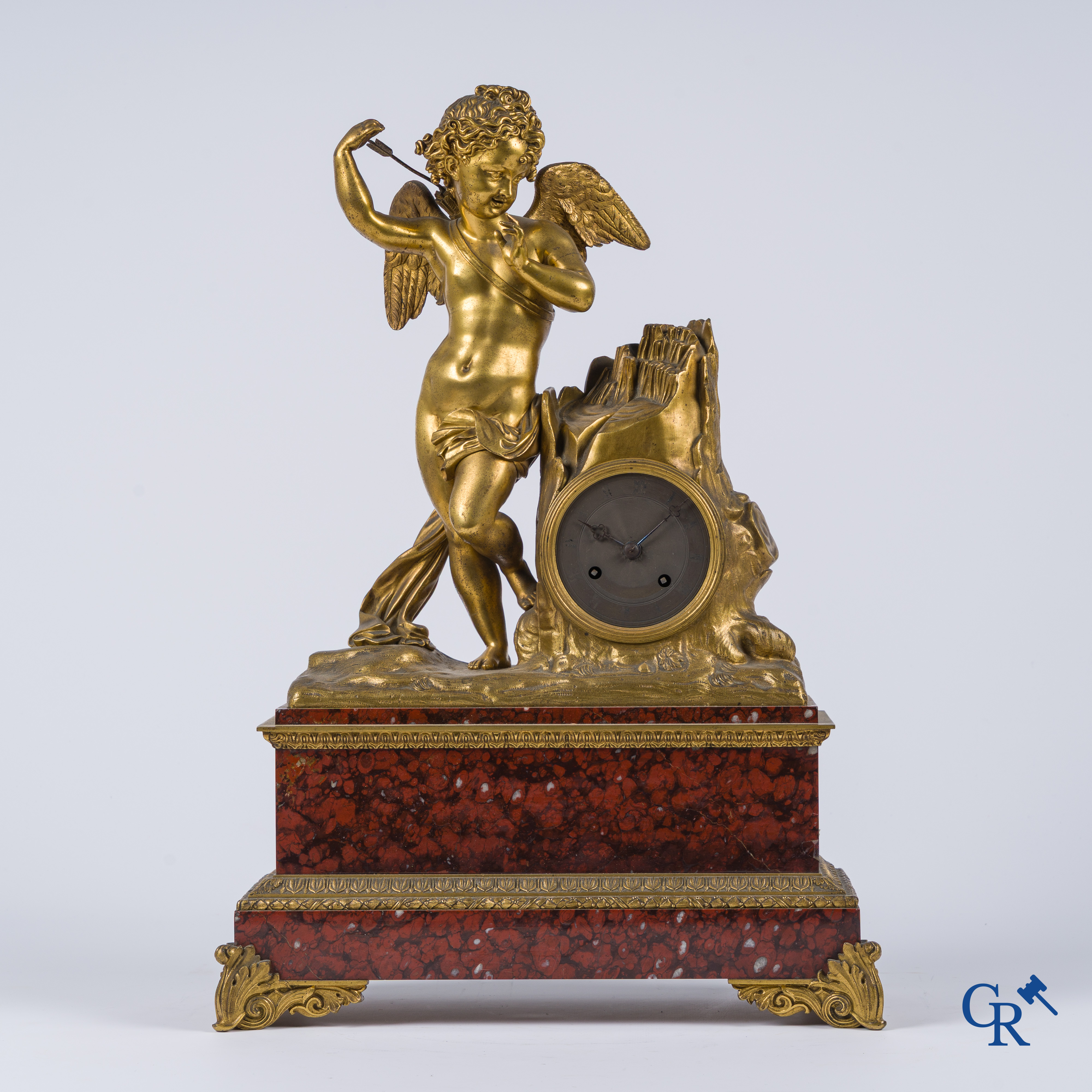 Charles X, een pendule met fijn geciseleerde cupido in verguld brons. Rood geaderde marmer sokkel. Circa 1840.
